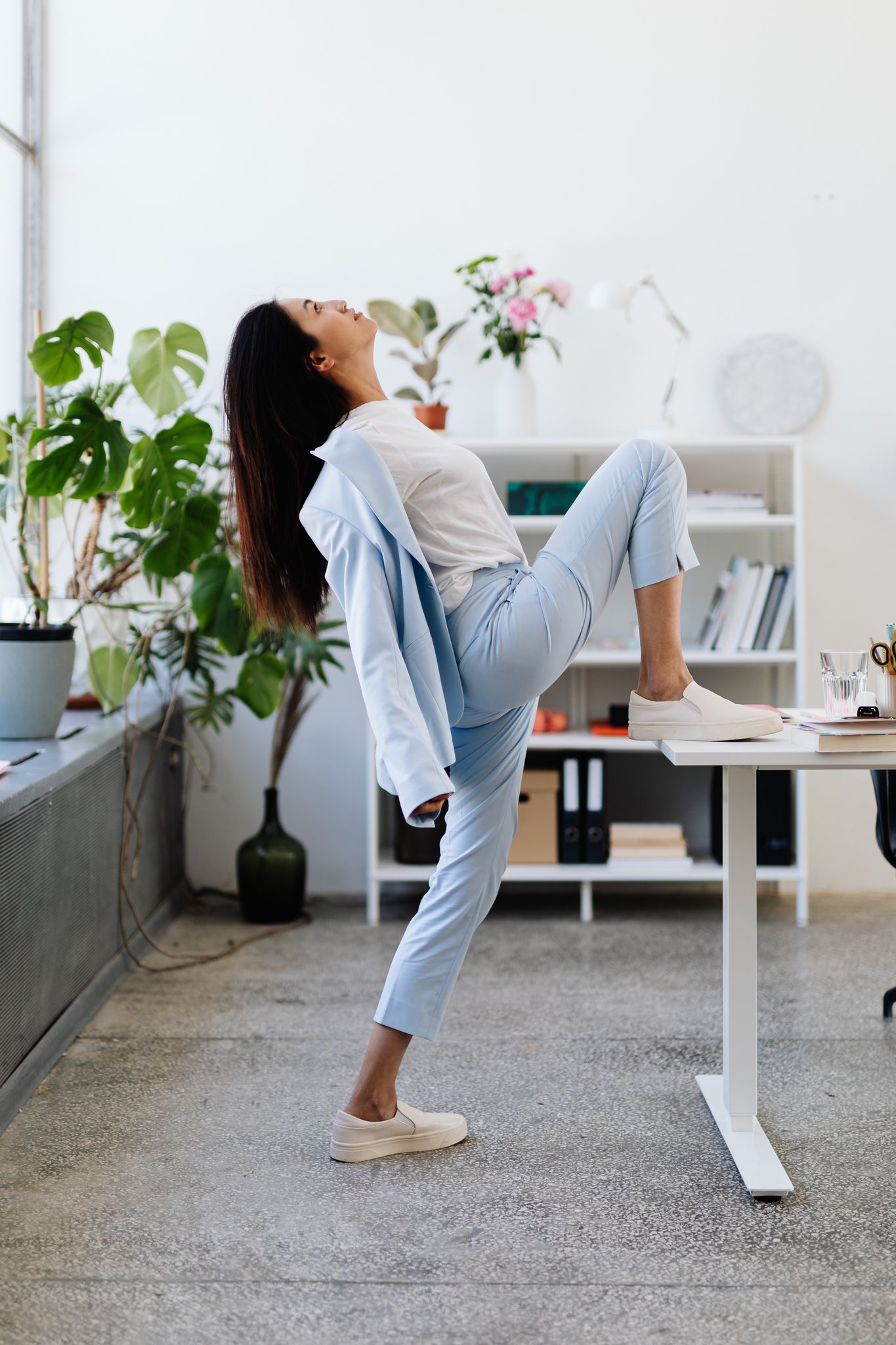 Business woman in blue suit stretching in bright office space, promoting workplace wellness.